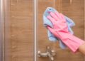 A hand wearing gloves is cleaning a shower glass