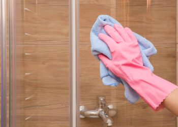 A hand wearing gloves is cleaning a shower glass