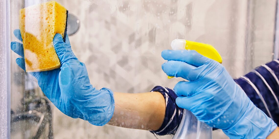 A person wearing gloves cleaning a shower glass