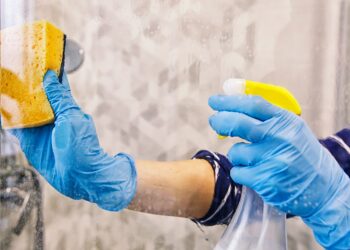 A person wearing gloves cleaning a shower glass