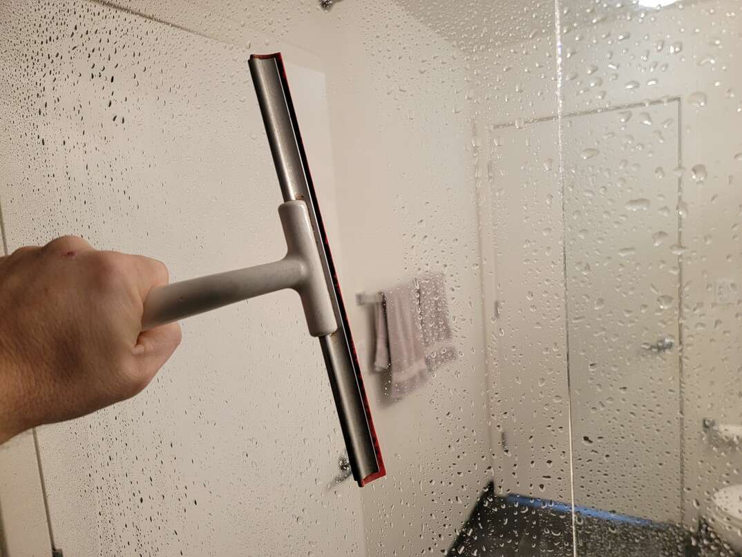 a person trying to remove soap scum from the shower glass